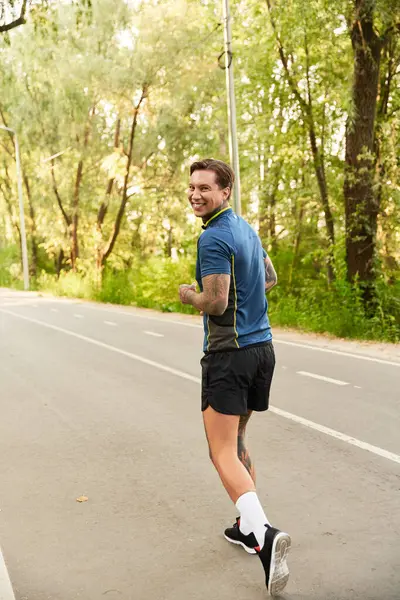 Neşeli genç bir adam yemyeşil bir parkın içinde ışıl ışıl gülümseyen sakin bir yürüyüş yapar..