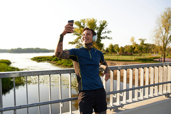A young man with tattoos takes a moment to capture his joyful reflection while walking.
