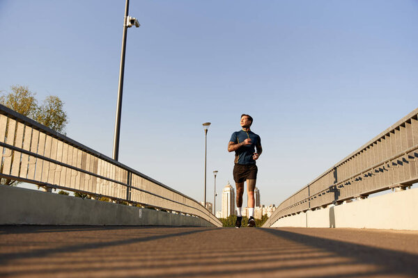 Красивый молодой человек уверенно идет по солнечной городской тропинке, окруженный видом на город.
