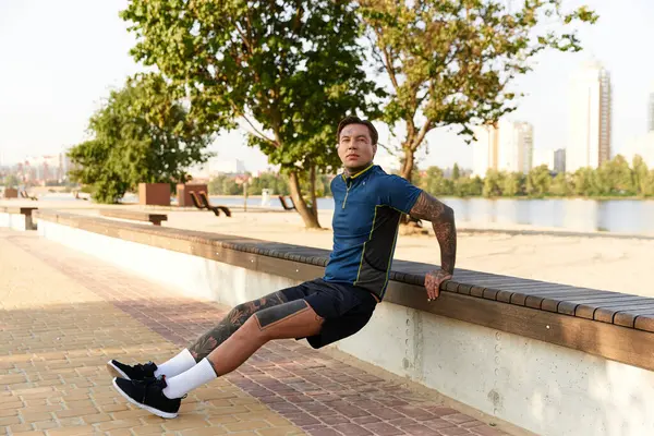 Dövmeli genç bir adam, sakin bir suyun yanında yürüyor, güneşin tadını çıkarıyor..