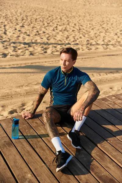 Yakışıklı genç bir adam, güneş batarken kumsalın yakınındaki ahşap bir güvertede oturuyor..