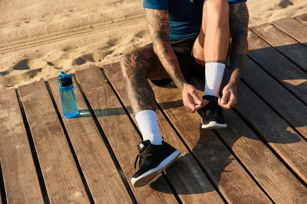 Şık bir genç adam plaj güvertesinde oturuyor, ayakkabılarını ayarlıyor ve günün tadını çıkarıyor..