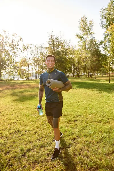 Parlak yeşil bir parkta gezinen genç adam spor malzemeleri ve gülümsemeler taşıyor..