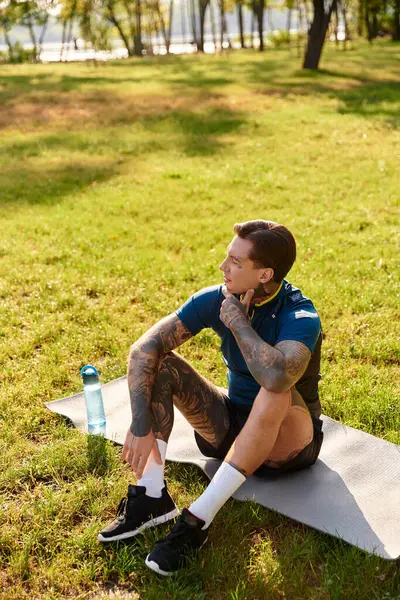 Genç bir adam güneşli bir parkta yeşillik içinde yürürken paspasın üzerinde dinlenmekten zevk alır..