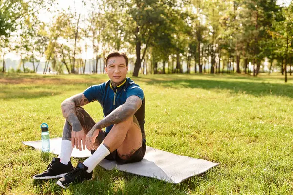 Serinletici bir yürüyüşten sonra canlı yeşil bir parkta paspasın üzerinde oturan yakışıklı genç adam..