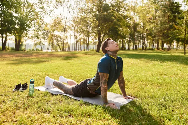 Genç, yakışıklı bir adam, ağaçlarla çevrili sakin bir parktaki çimlerin üzerinde yoga pozu alıyor..