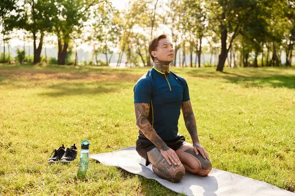 Genç bir adam dinlenme parkındaki yoga minderinde meditasyonda diz çöküp sıcak güneş ışığının tadını çıkarıyor..