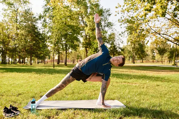 Genç adam güneşli, sakin yeşil bir parkta yoga pozu veriyor..