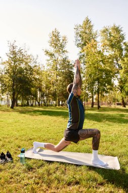 Yakışıklı genç bir adam yoga pozunda mindere uzanıyor, yemyeşil bir parkta güneşin tadını çıkarıyor..