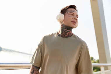 Dövmeleri olan genç bir adam su kenarında rahatça dolaşır, sıcak güneşin tadını çıkarır..