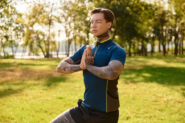 Dövmeli genç bir adam dışarıda, güneşin tadını çıkararak huzurlu bir yoga seansından hoşlanıyor..
