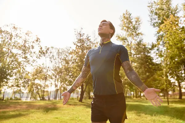 Dövmeleri olan genç bir adam canlı bir parkta yürüyor, sıcak güneş ışığının ve temiz havanın tadını çıkarıyor..