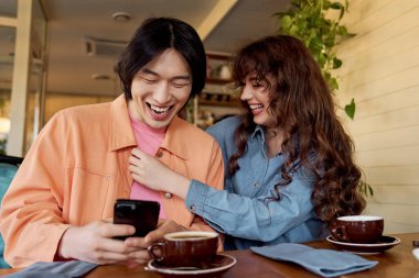 İki genç arkadaş kahveyi yudumlarken ve birlikte gülümserken keyifli bir anın tadını çıkarıyorlar..