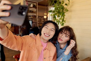 Genç arkadaşlar, hayat dolu bir kafe ortamında selfie çekerken gülüşlerini ve gülüşlerini paylaşırlar..