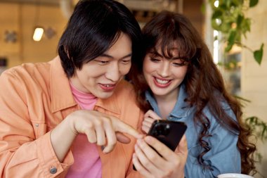 Çok kültürlü arkadaşlar bir kafede keyifli vakit geçiriyorlar, akıllı telefondan gülüyorlar..