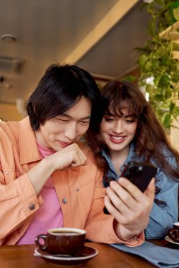 İki canlı arkadaş bir kafede oturup, akıllı telefonlarıyla birbirlerine bağlanırken neşeli bir gülümseme takınırlar..