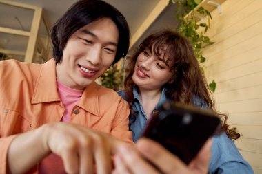 İki genç arkadaş bir kafede birlikte gülerken cep telefonlarında bir an paylaşıyorlar..