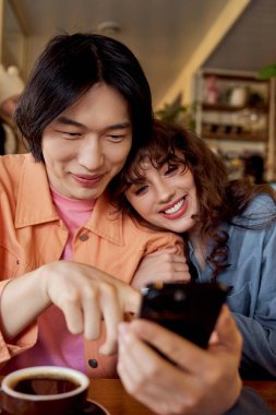 İki genç arkadaş bir kafede akıllı bir telefona bakarken neşe içinde gülüyorlar..