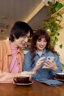 İki genç arkadaş bir kafede telefonlarını incelerken keyifli bir anı paylaşıyorlar..