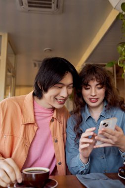 Sıcak bir kafede, genç bir Asyalı adam ve beyaz bir kadın telefona bakarken kahkahalar atıyorlar..