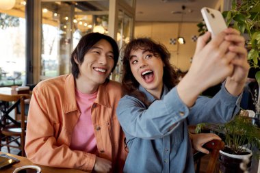 İki çok kültürlü arkadaş, neşeli bir kafede eğlenceli bir selfie çekerken aynı kahkahayı paylaşıyorlar..