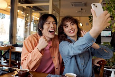 İki genç arkadaş, canlı bir kafe ortamında selfie çekerken mutlu bir anı paylaşıyorlar..