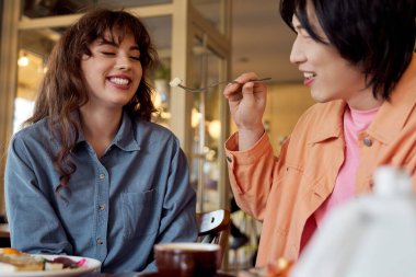 Genç bir Asyalı, neşeli arkadaşını sıcak bir kafede neşeyle besler..