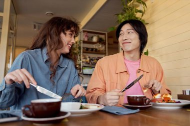 İki genç arkadaş sıcak bir kafe ortamında keyifli sohbetler ve lezzetli yemekler yapıyorlar..