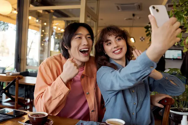 İki genç arkadaş, canlı bir kafe ortamında selfie çekerken mutlu bir anı paylaşıyorlar..