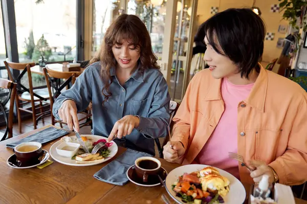 Genç bir Asyalı erkek ve kadın canlı bir kafede kahkahalarını içerken yemeklerini yiyorlar..