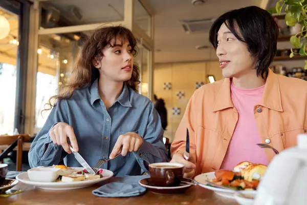 Canlı bir kafede, iki çok kültürlü arkadaş keyifli bir brunch 'ın ve iç açıcı bir sohbetin tadını çıkarırlar..
