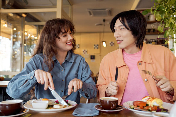 Two young friends sharing a joyful meal together in a vibrant cafe setting.