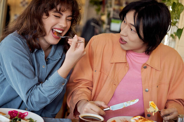 Two young friends enjoy a delightful moment together while sharing food in a vibrant cafe.