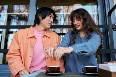 Genç bir Asyalı erkek ve kadın, canlı bir kafede kahve içerken neşeli bir bağ kurarlar..