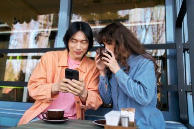 Sıcak bir kafede, genç bir çok kültürlü ikili kahkaha atarak kahkaha atıyor ve telefonları kontrol ediyor..