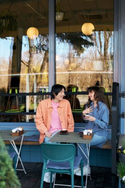İki genç arkadaş, doğal ışıkla dolu canlı bir kafede canlı bir sohbetin tadını çıkarıyorlar..