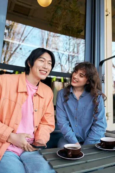 İki arkadaş kahkahalarını ve sıcak içkilerini güneşli bir kafede paylaşıyor, farklılıklarını kutluyorlar..