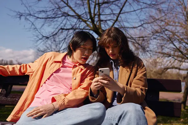 Genç Asyalı bir adam ve kadın canlı bir parkta telefona bakıyorlar..