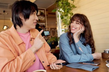 Genç bir Asyalı erkek ve kadın, yerel bir kafede kahkaha ve neşe paylaşıyor, arkadaşlığı kucaklıyor..