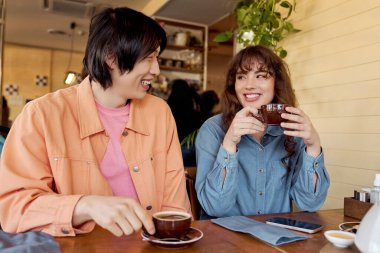 Canlı bir kafede, genç bir Asyalı adam ve çok kültürlü bir kadın kahveyi ve gülümsemeyi paylaşıyor..