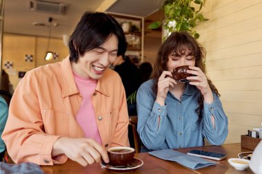 Genç Asyalı bir adam, keyifle kahkaha atar. Arkadaşı, sıcak bir kafede kahvenin tadını çıkarırken..