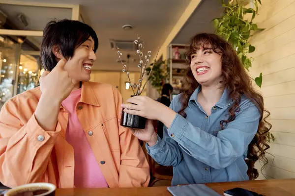 İki çok kültürlü arkadaş sıcak bir kafede keyifli bir anın tadını çıkarırlar, karşılıklı gülüşürler..