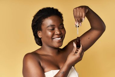 Gülümseyen genç bir kadın, sıcak sarı bir zemine cilt serumu sürmekten zevk alır..