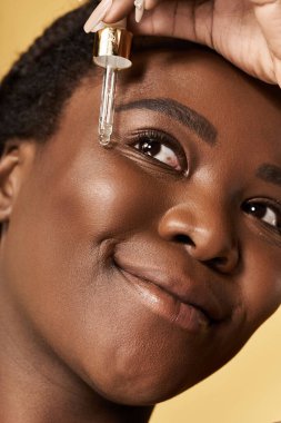 Parlak stüdyo genç siyahi bir kadının mutlu bir şekilde cilt bakımı yaptığını gösteriyor..