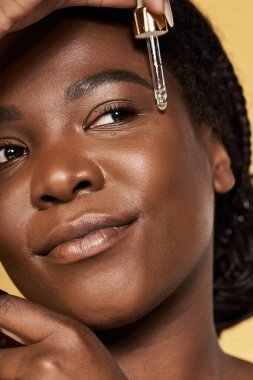 Genç Afrikalı Amerikalı kadın serum uyguluyor, parlayan cilt ve güzellik ayinleri sergiliyor..