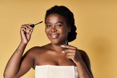 Genç siyahi bir kadın stüdyoda parlak cildini güzellik ürünüyle ön plana çıkarıyor..