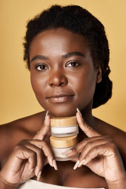 Stüdyoda, genç siyah bir kadın kusursuz cildini güzellik ürünleriyle sergiliyor..