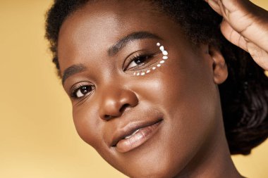 Parlak ten, genç bir Afrikalı Amerikalı kadının üzerine parlıyor. Stüdyo ortamında güven içinde poz veriyor..