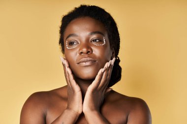 Genç Afrikalı Amerikalı kadın, sıcak bir fon çerçevesi ile çerçevelenirken parlak bir ten sergiliyor..