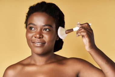 Genç bir Afrikalı Amerikalı kadın parlak bir stüdyoda fırçayla makyaj yapıyor..